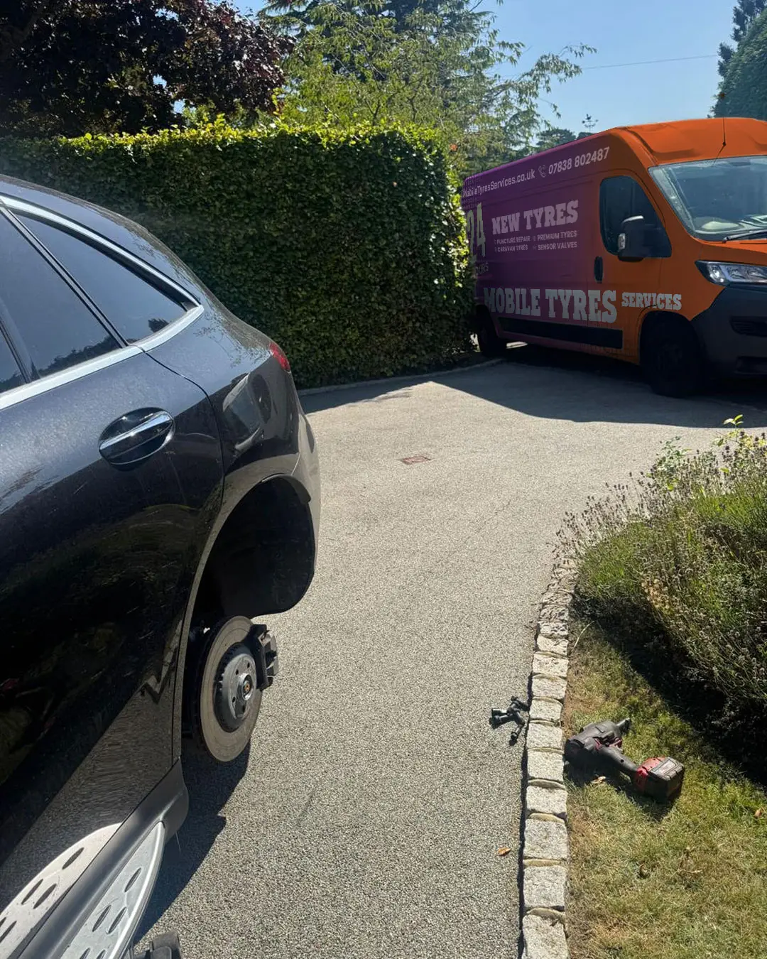 Orange tyre-fitting van parked behind a car with its wheel removed on a residential drive