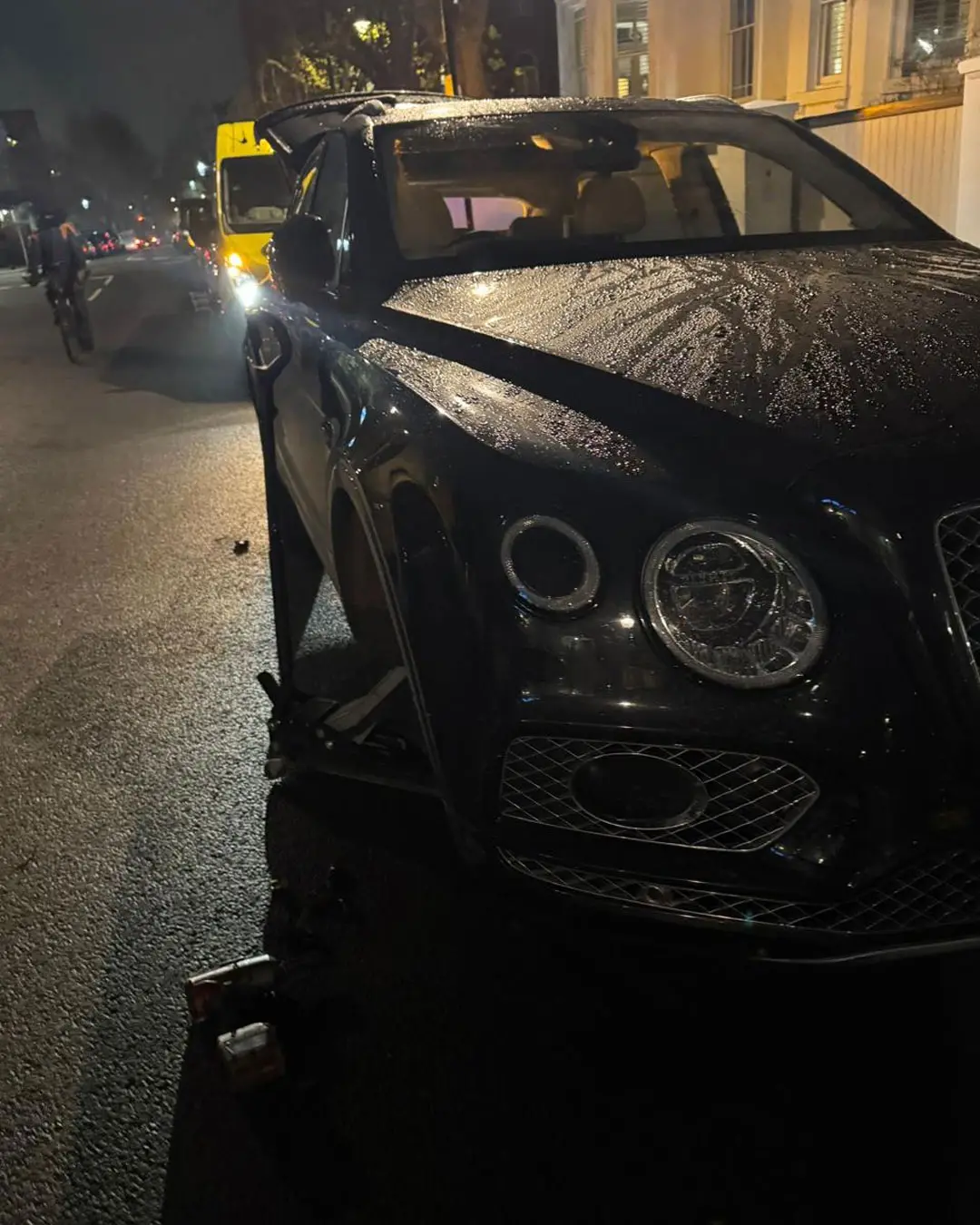 Close-up of a black Bentley at night with the wheel removed and the van’s work lights on