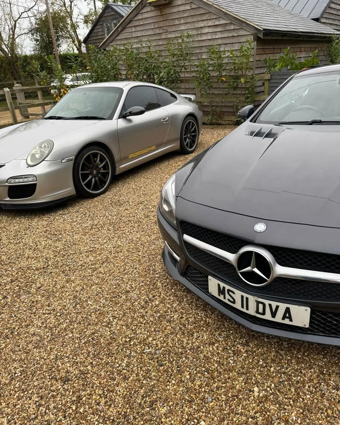 Silver Porsche 911 and grey Mercedes SL on a gravel drive